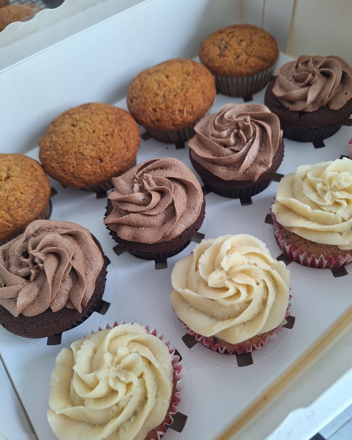 A boxed assortment of muffins and frosted cupcakes