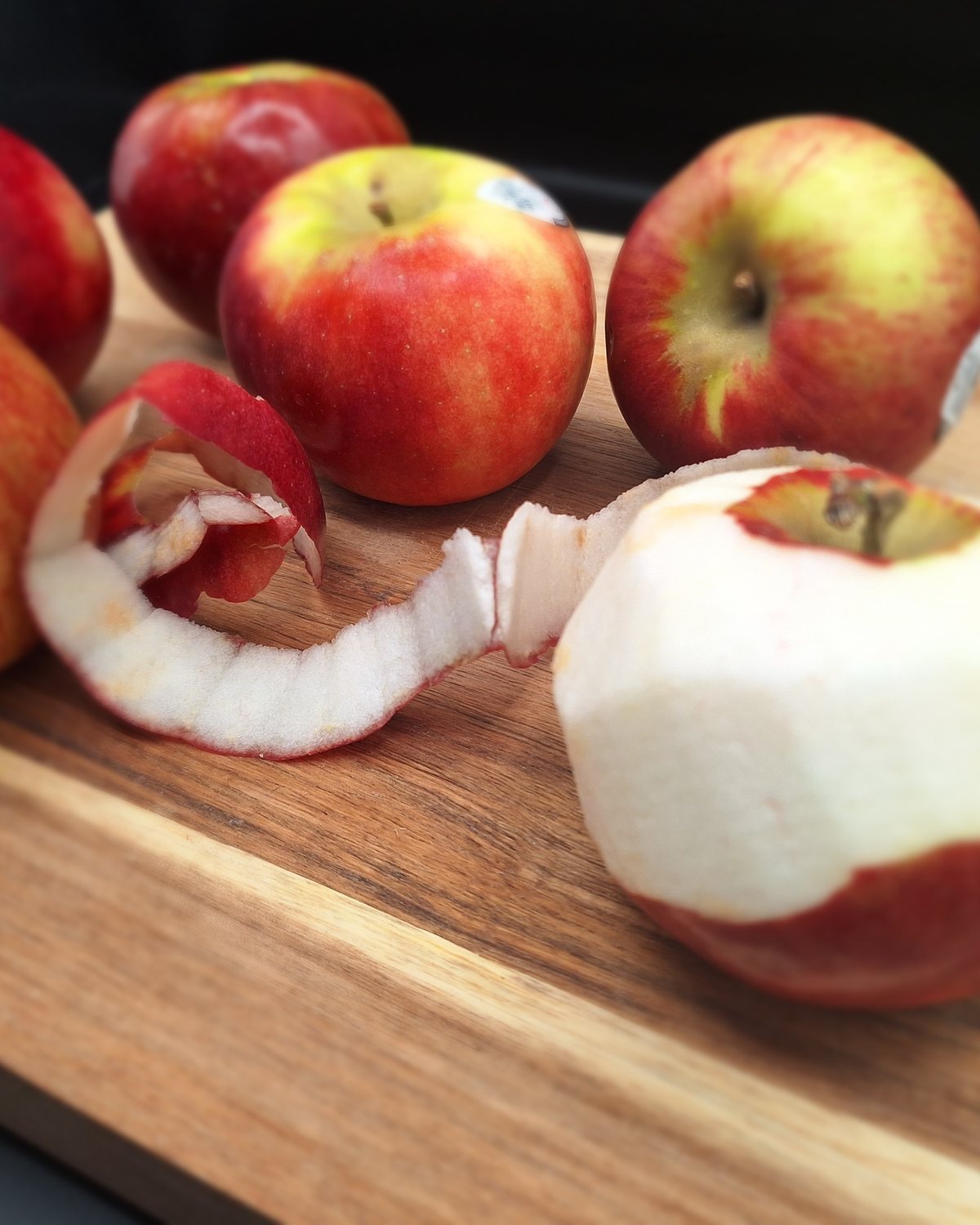 Apples being peeled by hand on a wooden board