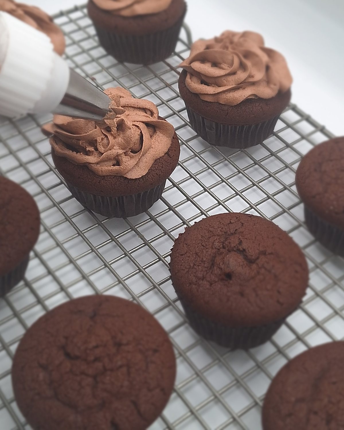 Chocolate frosting being piped onto a cupcake by hand